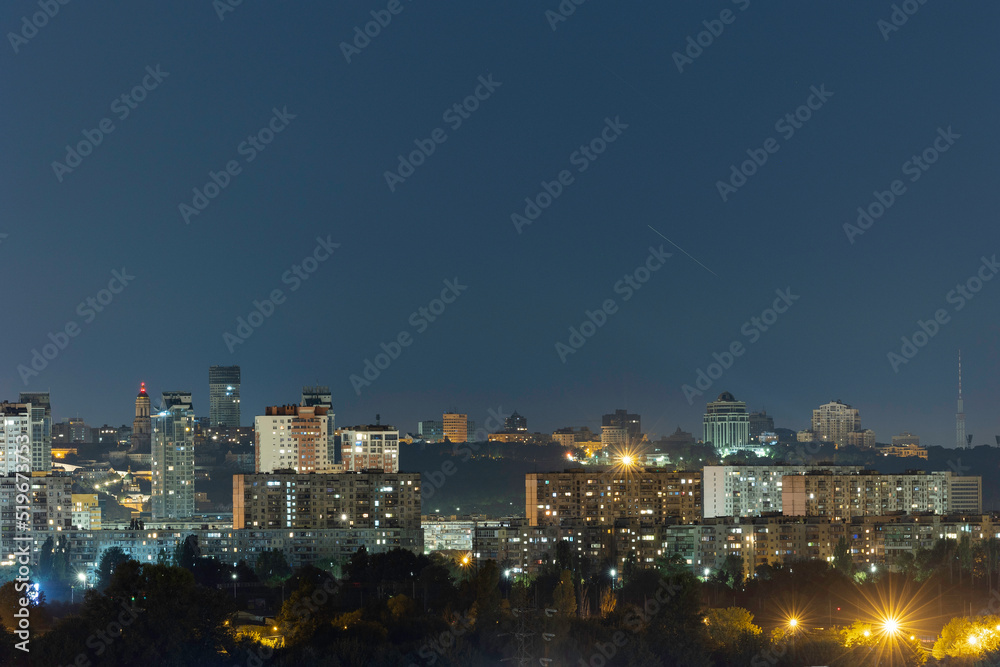 Fototapeta premium Night cityscape of the big city. Awesome bright, multi colored light at curfew on empty streets. Apartment buildings in bedroom community, commuter town area. Kyiv in last days in july 2022. Ukraine.