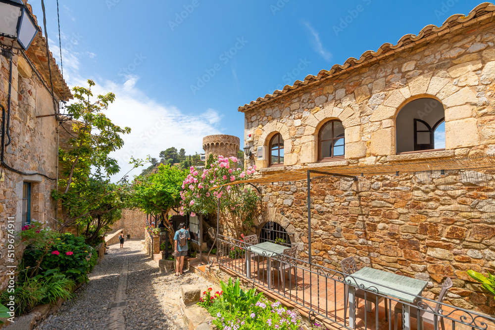 Obraz premium A picturesque cobblestone street with cafes and shops in the historic medieval hilltop 12th century castle in the Costa Brava seaside town of Tossa de Mar., Spain.
