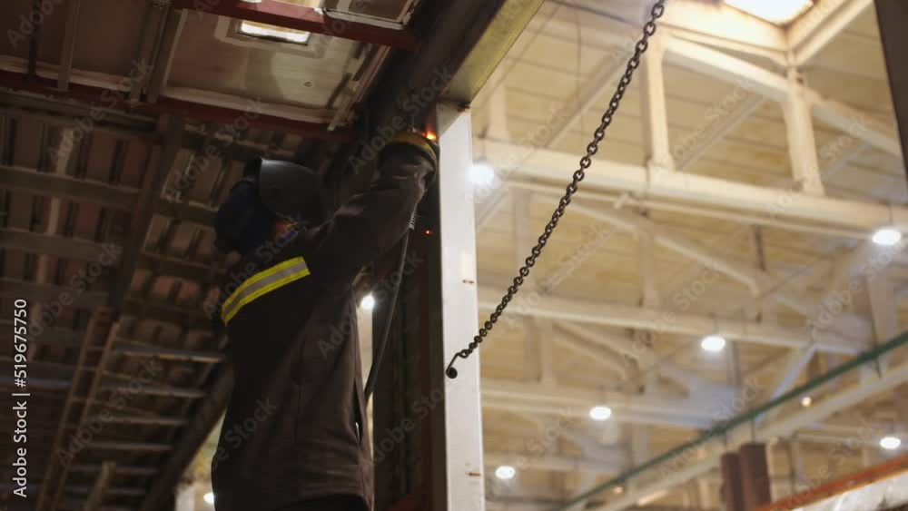 Close-up view from the bottom to factory laborer in protective suit and safety mask using a welding torch for steel structures. welding process with sparks. Close-up view from the bottom to factory laborer in protective suit and safety mask using a welding torch for steel structures. welding process with sparks.