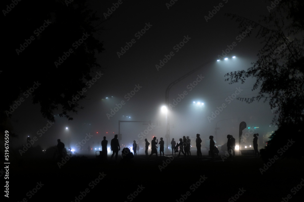 Siluetas difusas de gente en el parque de la ciudad en la noche con niebla
