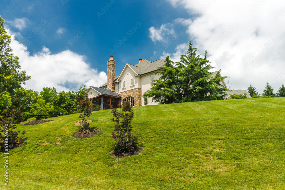 Beautiful exterior of a luxury home on a hill. Yard with green grass and trees.