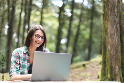 Young latin woman sitting in the forest working with laptop freelancing camera laptop smiling at Costa Rica