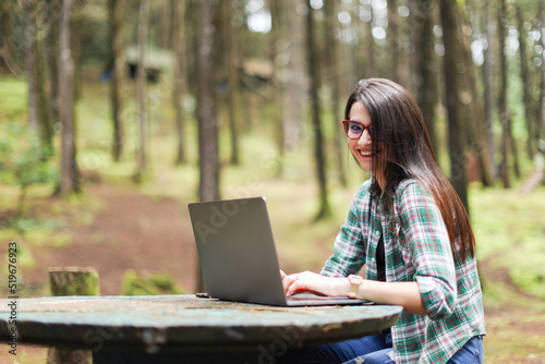 Young latin woman sitting in the forest working with laptop freelancing looking camera smiling at Costa Rica. 