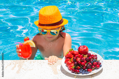 Little child by the pool eating fruit and drinking lemonade cocktail. Summer kids vacation concept.