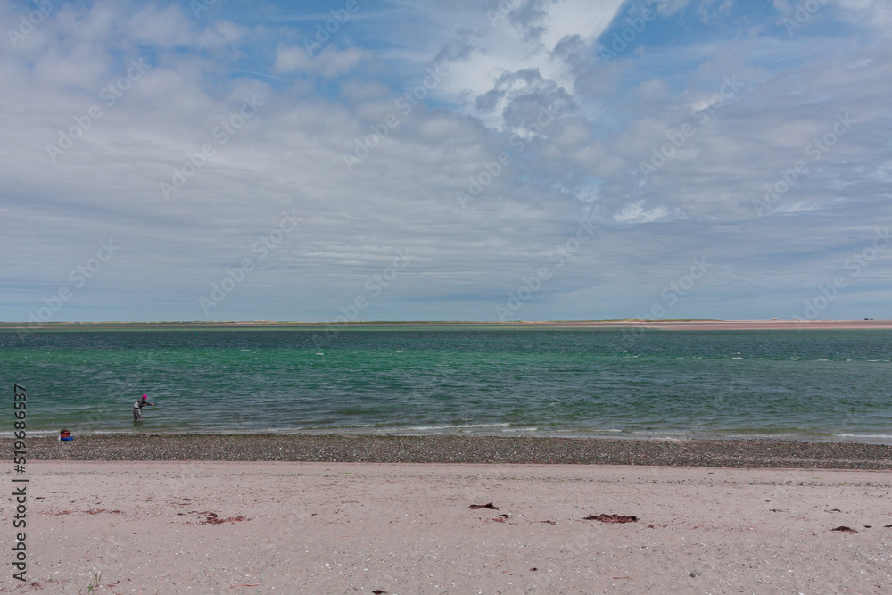 Wide View Of A Beach With A Fisherman Under A Cloudy Sky