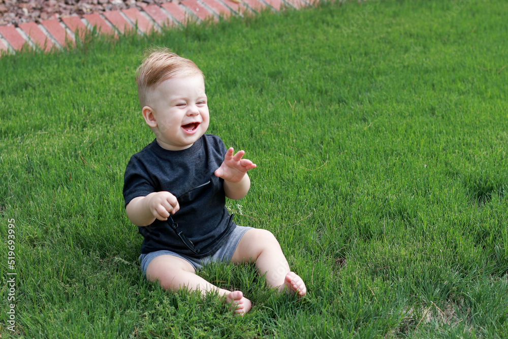 little baby boy sitting on green grass, playing and laughing little baby boy sitting on green grass, playing and laughing