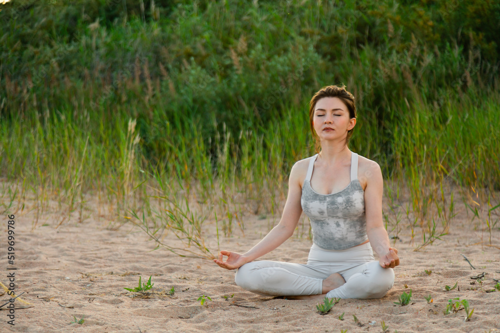 Woman practicing yoga outside in lotus pose on sand