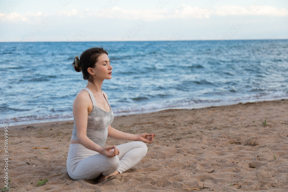 Woman practicing yoga outside in lotus pose on beach