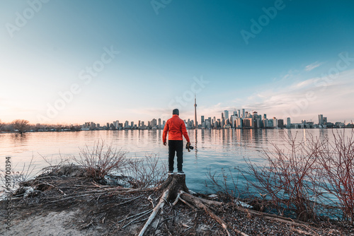 Man with a red jacket standing and facing the Toronto city skyline at Ontario, Canada