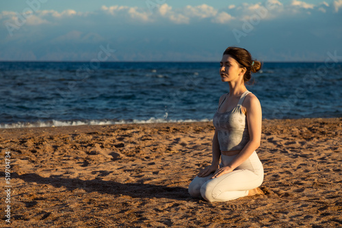 Woman practicing yoga outside in hero pose on beach, meditating in the sunset
