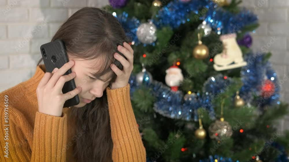 Bad telephone call for New year. A teen girl receive a stressed call on her smartphone by the decorated tree during Christmas night. Bad telephone call for New year. A teen girl receive a stressed call on her smartphone by the decorated tree during Christmas night.