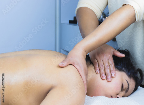 Relaxed young brunette latina woman receiving a decontracting oil massage in a spa salon photo