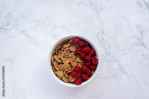 Bowl of multigrain cereal with fresh raspberry berries on marble table background. Healthy diet breakfast. Top view, copy space