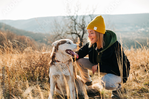 Fotografie Young woman and her husky dog trek down a forest trail offering a scenic view of the trees changing colors