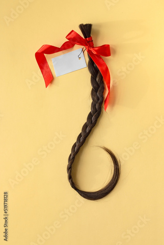 Long brown braid with red ribbon and empty label on yellow background, haircut selling service, material of natural hair for model hairstylish extension, top view, vertical image