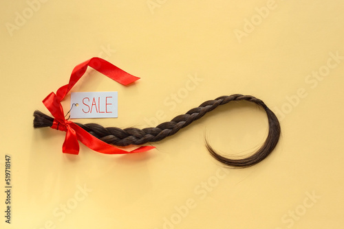 Long brown braid with tag label and red ribbon on yellow background, haircut sale service, material of natural hair for model hairstylish extension, top view