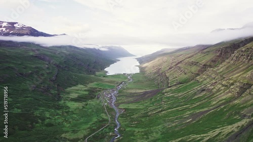 Exploring at Fjord Mjóifjörður with fog over ocean and dirt road and natural waterfall flowing in the valley in East of Iceland photo