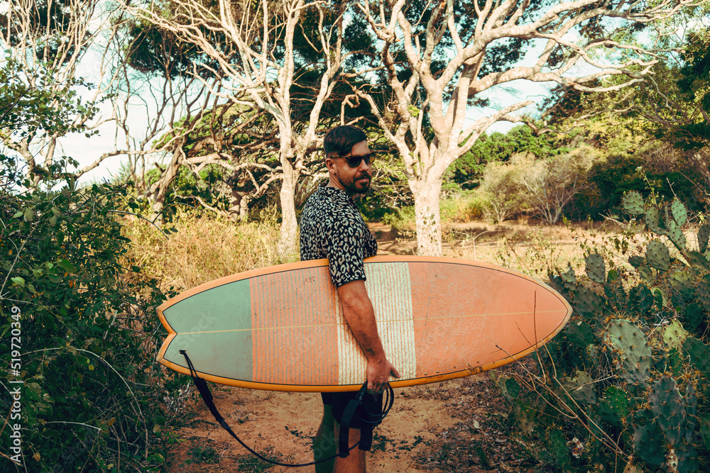 Mężczyzna surfer z deską surfingową, idący wybrzeżem na tle jungle, aktywny wypoczynek. - obrazy, fototapety, plakaty 