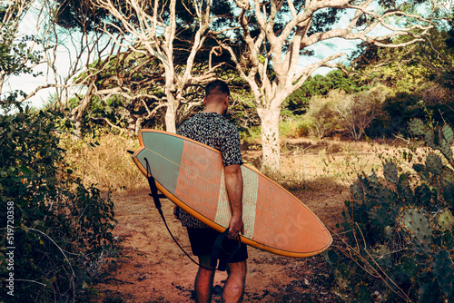 Obraz na płótnie Mężczyzna surfer z deską surfingową, idący wybrzeżem na tle jungle, aktywny wypoczynek. w salonie
