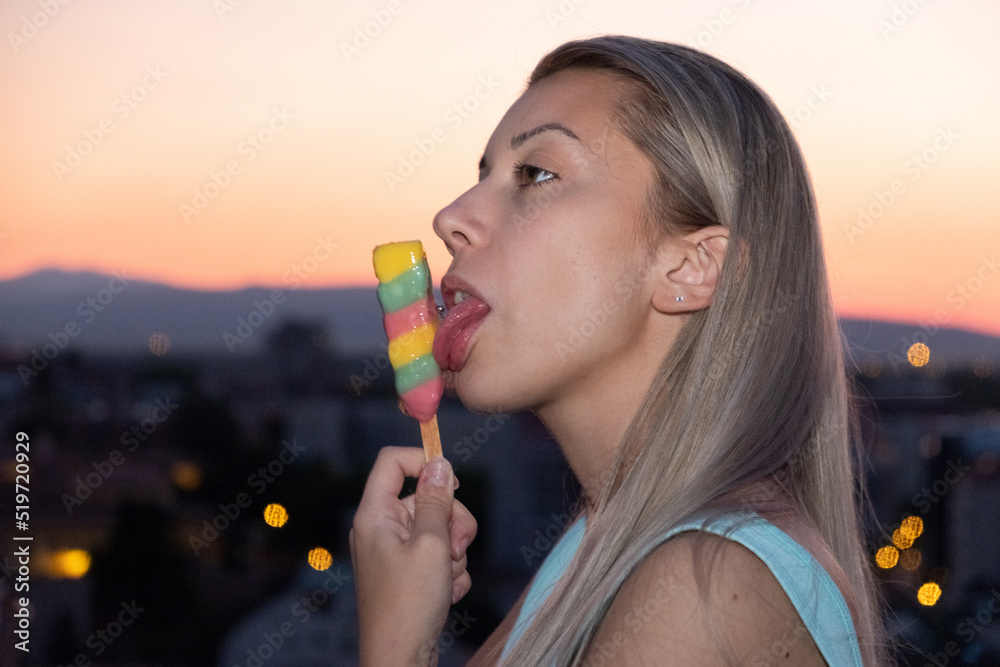 Sexy young woman eating ice cream on a rooftop of a building at orange summer sunset in the city Sexy young woman eating ice cream on a rooftop of a building at orange summer sunset in the city