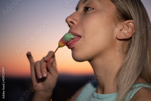 Closeup portrait of a young woman licking ice cream at summer sunset in the city