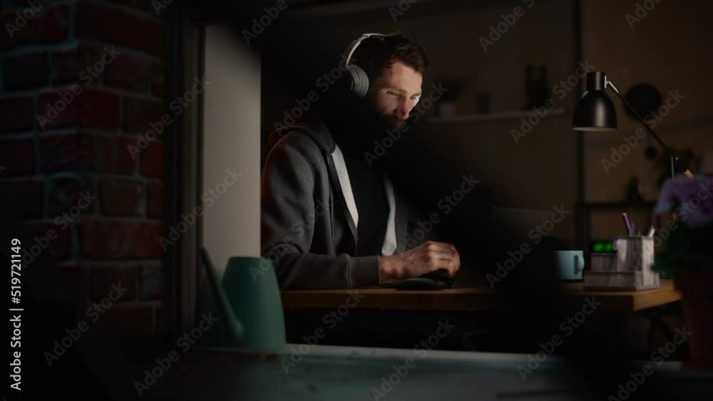 Happy Software Developer Working on a Laptop. Cheerful Information Technology Specialist Wearing Headphones, Listens to Music, Does Professional Work. Remote Job at Home Office Concept. Happy Software Developer Working on a Laptop. Cheerful Information Technology Specialist Wearing Headphones, Listens to Music, Does Professional Work. Remote Job at Home Office Concept.