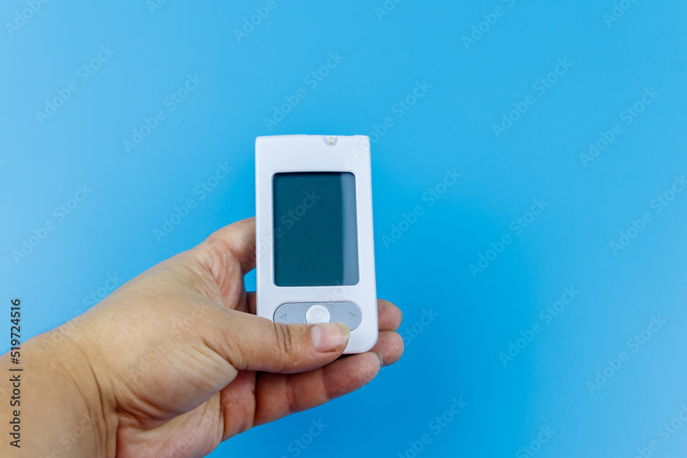 Digital glucometer in female hand over a pastel blue background. Diabetes concept Digital glucometer in female hand over a pastel blue background. Diabetes concept