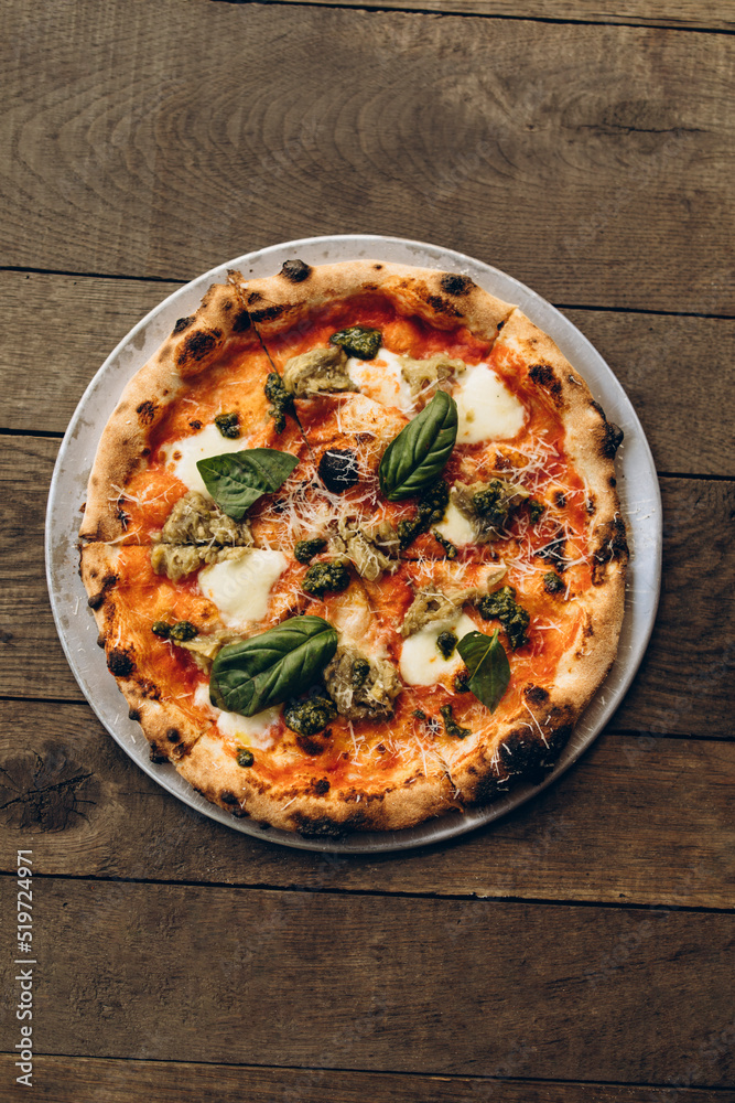 italian pizza with burnt sides on a wooden background top view. pizza with pesto sauce, mozzarella and basil leaves. sliced pizza close-up
