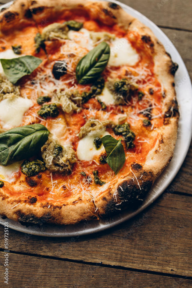 italian pizza with burnt sides on a wooden background top view. pizza with pesto sauce, mozzarella and basil leaves. sliced pizza close-up italian pizza with burnt sides on a wooden background top view. pizza with pesto sauce, mozzarella and basil leaves. sliced pizza close-up