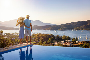 Loving couple on vacation time enjoys the summer sunset over the Aegean Sea by the swimming pool, Greece