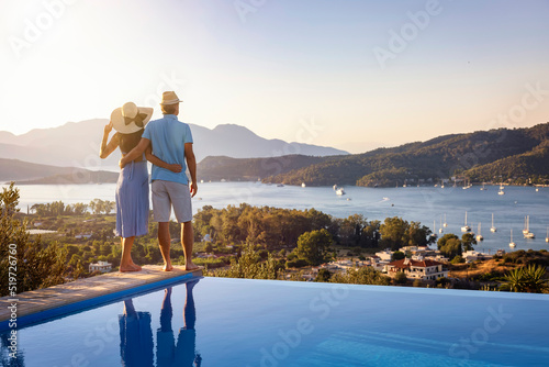 Loving couple on vacation time enjoys the summer sunset over the Aegean Sea by the swimming pool, Greece