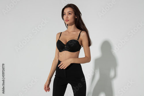 Portrait of a beautiful brunette young woman dressed in a black bra and pants, isolated black background.