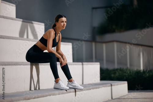Sporty and fit woman sitting on the street  relaxing after nice workout session