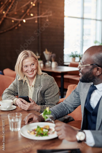 Mature businesswoman smiling to her colleague during their conversation at business lunch at the restaurant