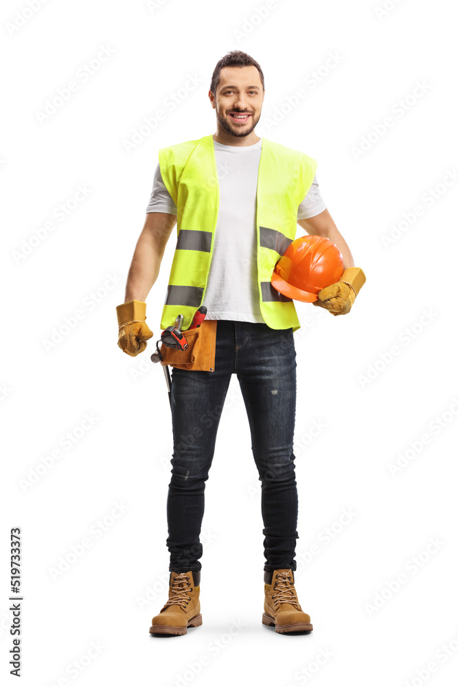 Full length portrait of a construction worker holding a helmet, wearing a tool belt and smiling at camera Full length portrait of a construction worker holding a helmet, wearing a tool belt and smiling at camera