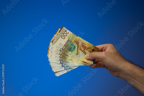 A spread mix of 200 and 100 Swiss Francs banknotes, held in hand by a Caucasian male. Close up studio shot, isolated on blue background