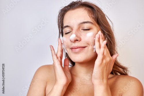 A girl applies foam on her face to clean her skin. Face care concept.