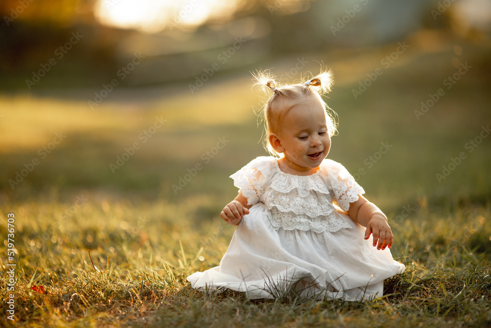 Happy little girl sits on the grass outdoors. Cute baby girl with blond hair is walking in park. Adorable kid play with grass. concept of happy childhood, games, fun. Family leisure. outdoor play Happy little girl sits on the grass outdoors. Cute baby girl with blond hair is walking in park. Adorable kid play with grass. concept of happy childhood, games, fun. Family leisure. outdoor play