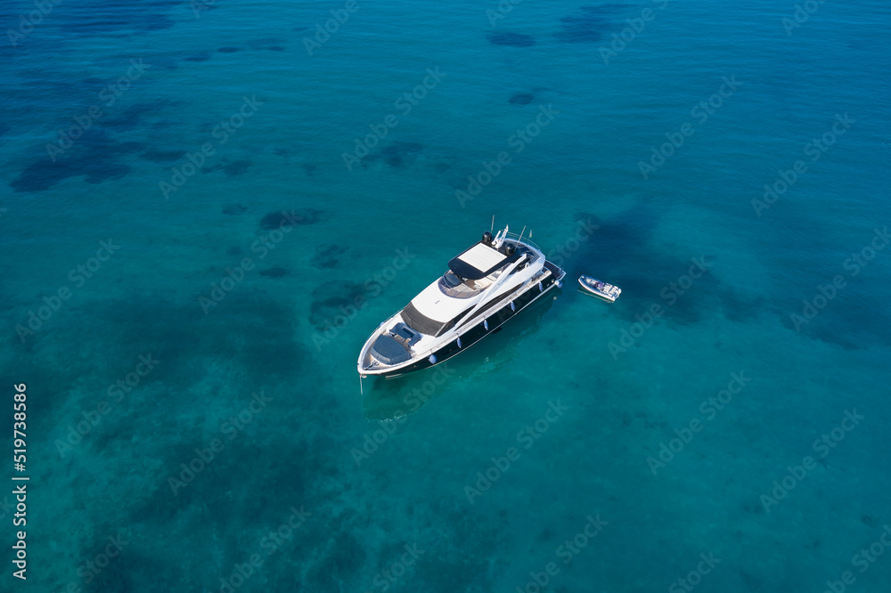 White yacht on transparent blue water top view. White yacht at anchor aerial view. White boat on transparent water, top view.