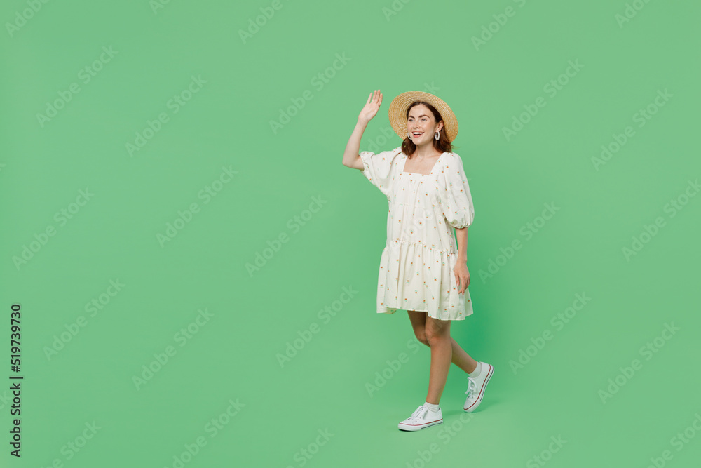 Full body side view young happy smiling fun cheerful woman she 20s in white dress hat walking go waving hand isolated on plain pastel light green background studio portrait. People lifestyle concept Full body side view young happy smiling fun cheerful woman she 20s in white dress hat walking go waving hand isolated on plain pastel light green background studio portrait. People lifestyle concept