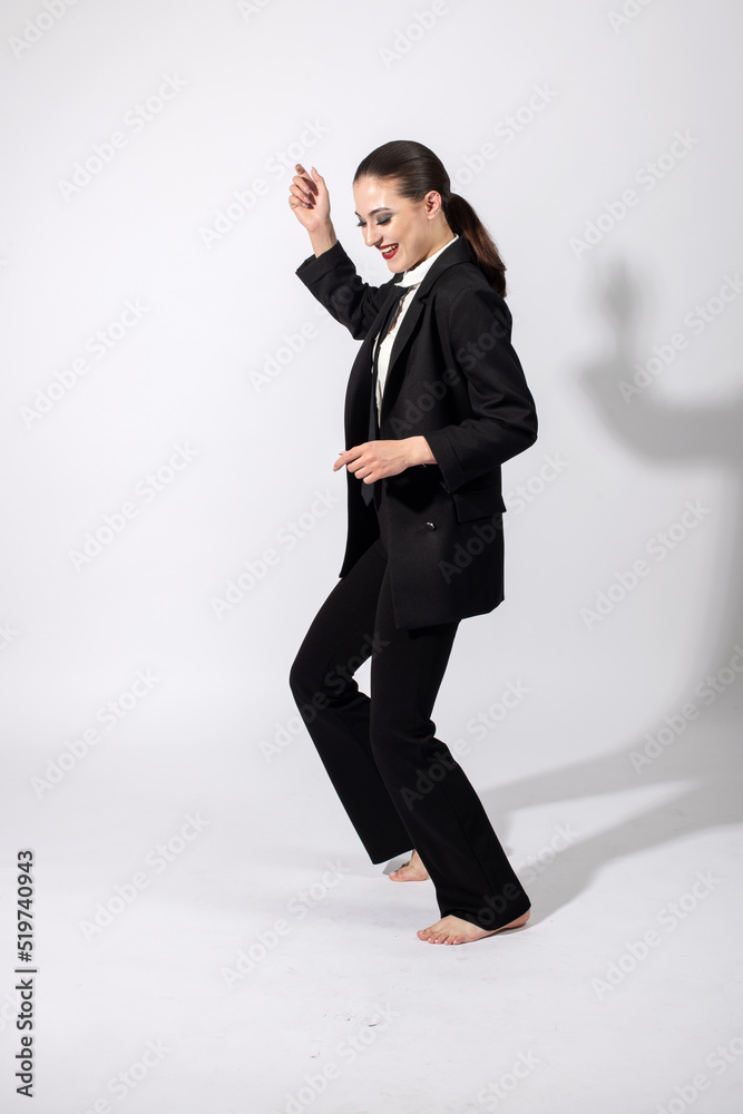 Happy with smile beautiful woman wearing classic black suit, white shirt and black tie dancing with bare feet on white studio background with copy space. Model with ponytail hairstyle