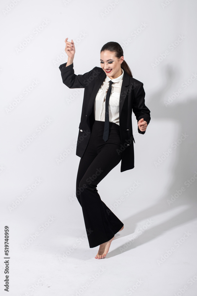Happy with smile beautiful woman wearing classic black suit, white shirt and black tie dancing with bare feet on white studio background with copy space. Model with ponytail hairstyle Happy with smile beautiful woman wearing classic black suit, white shirt and black tie dancing with bare feet on white studio background with copy space. Model with ponytail hairstyle