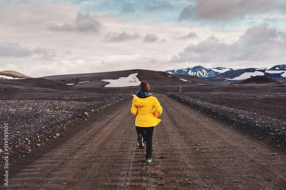Asian woman in yellow jacket running on dirt road at highlands of iceland