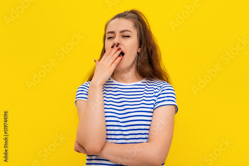 Young attractive woman wearing in white-blue striped t shirt feeling tired after night without sleep, yawning, covering opened mouth with palm. Restless and sleepiness