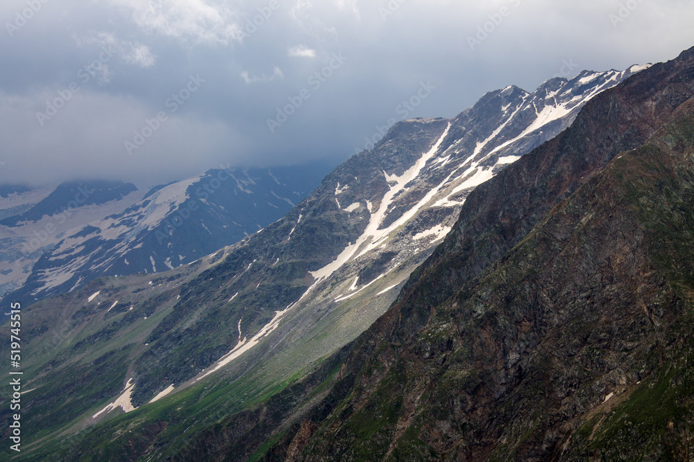 Obraz premium Panoramic landscape - silhouette of the top of a high mountain with glaciers and white snow and cloudy blue sky in the Elbrus region in the northern Caucasus in Russia