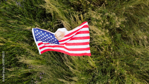 full length blond Woman holding American Flag in trees shadow of sunlight Back view cute blondy girl run on fresh green grass texture