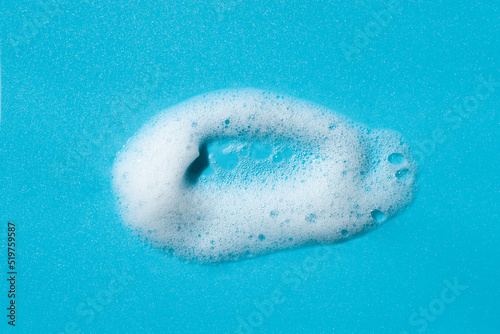 Foam swatch on a blue background. Soapy liquid texture with bubbles. Natural sunshine and shadows. Skin care cleansing cosmetic in top view.