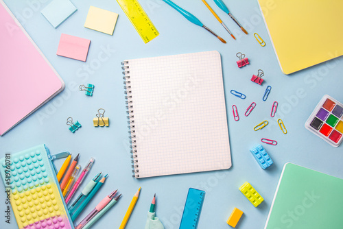 The concept of back to school. School supplies and stationery in pastel colors lie on a blue background in the form of a frame.