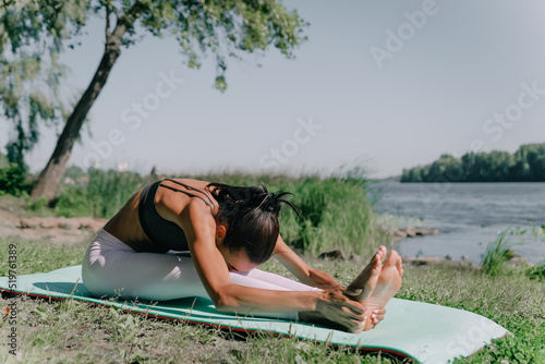 young African woman sitting in nature near the river stretching her legs in bright sunlight
