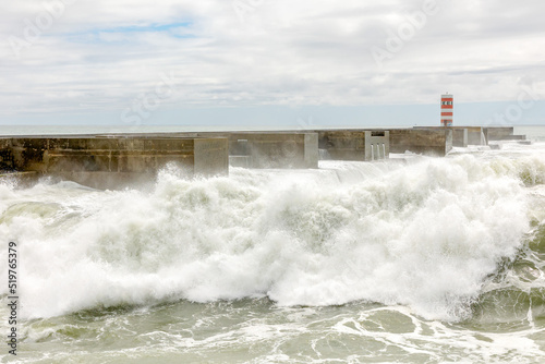 Waves crashing against the harbour wall in Porto, Portugal, Europe. Lighthouse in view, space for text, showing strength, natural power and ferocity of the sea 17 MAY 2022